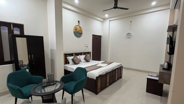 A hotel room with a bed, two chairs, a small table, a ceiling fan, a clock, and a wardrobe. - Shri Awadh Hotel (Sitamarhi)
