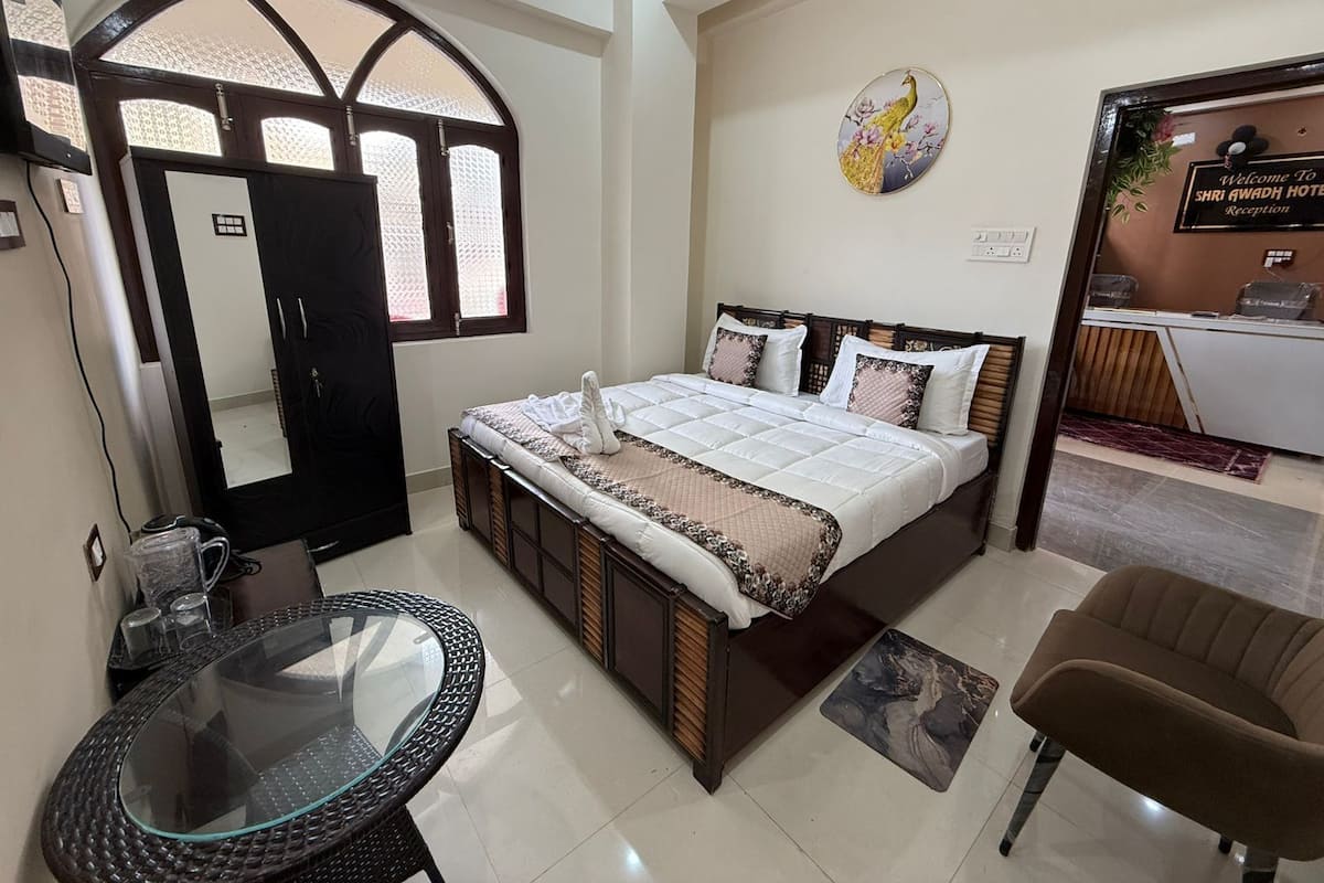 Habitación de hotel con cama, una mesita de vidrio redonda, un sillón marrón y un mostrador de recepción con un cartel.