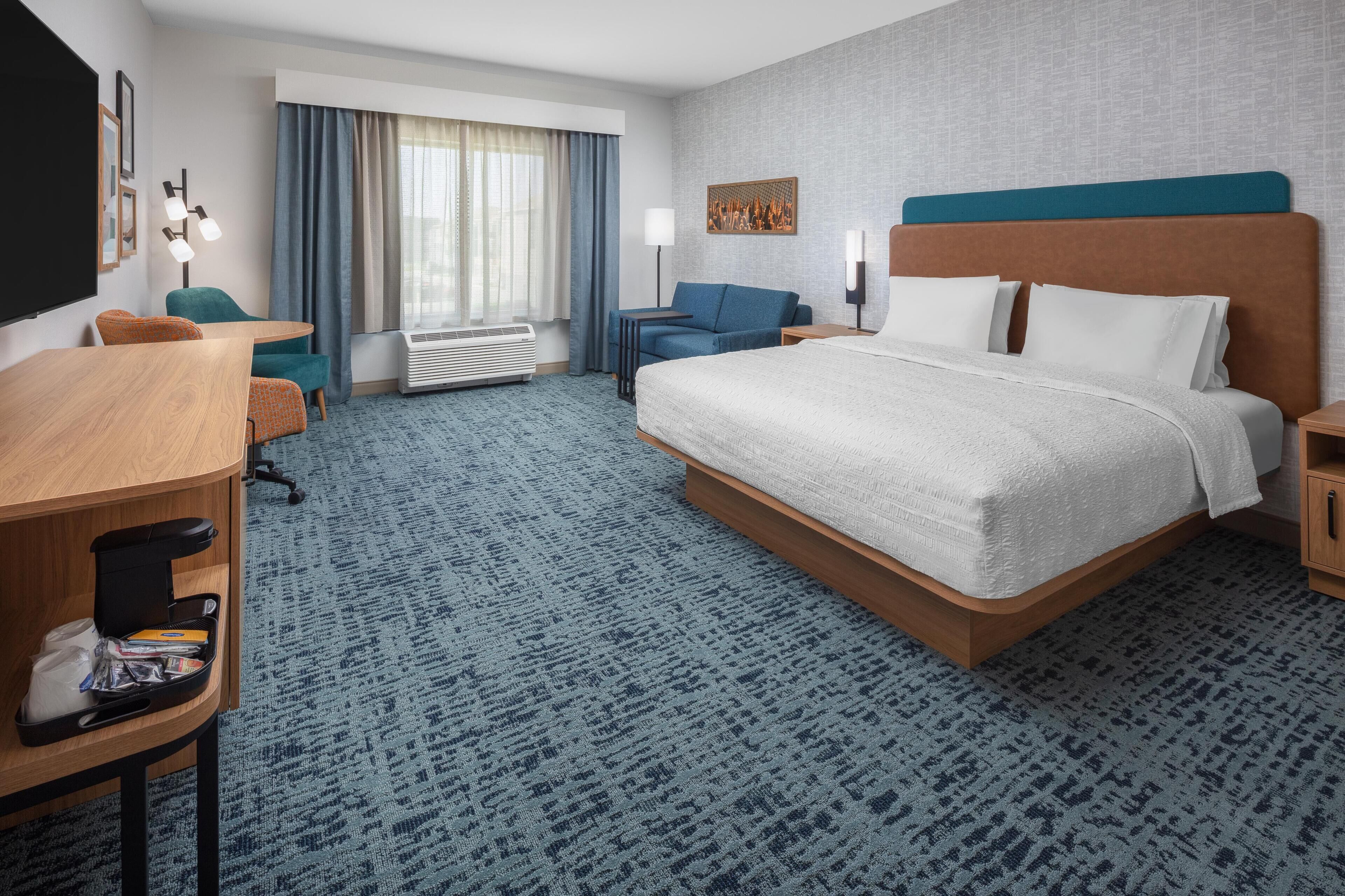 Una habitación de hotel con una cama grande, un escritorio, una silla, un sofá y una ventana con cortinas.