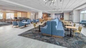 A modern hotel lobby with a long blue seating area, multiple tables, and a reception desk. - Hampton Inn by Hilton Grand Island Medical Center (Grand Island)
