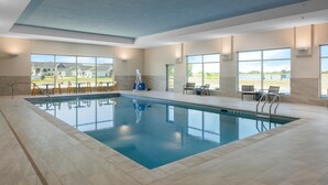 A large indoor swimming pool with clear views of the outside, surrounded by tiled flooring and equipped with sun loungers and chairs. - Hampton Inn by Hilton Grand Island Medical Center (Grand Island)