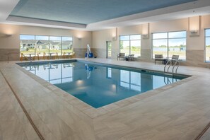 Una amplia piscina interior con vistas despejadas al exterior, rodeada de suelo de baldosas y equipada con tumbonas y sillones.