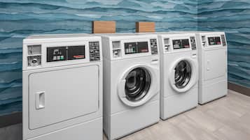 A row of white front-loading washers with digital displays, set against a blue wavy wall.