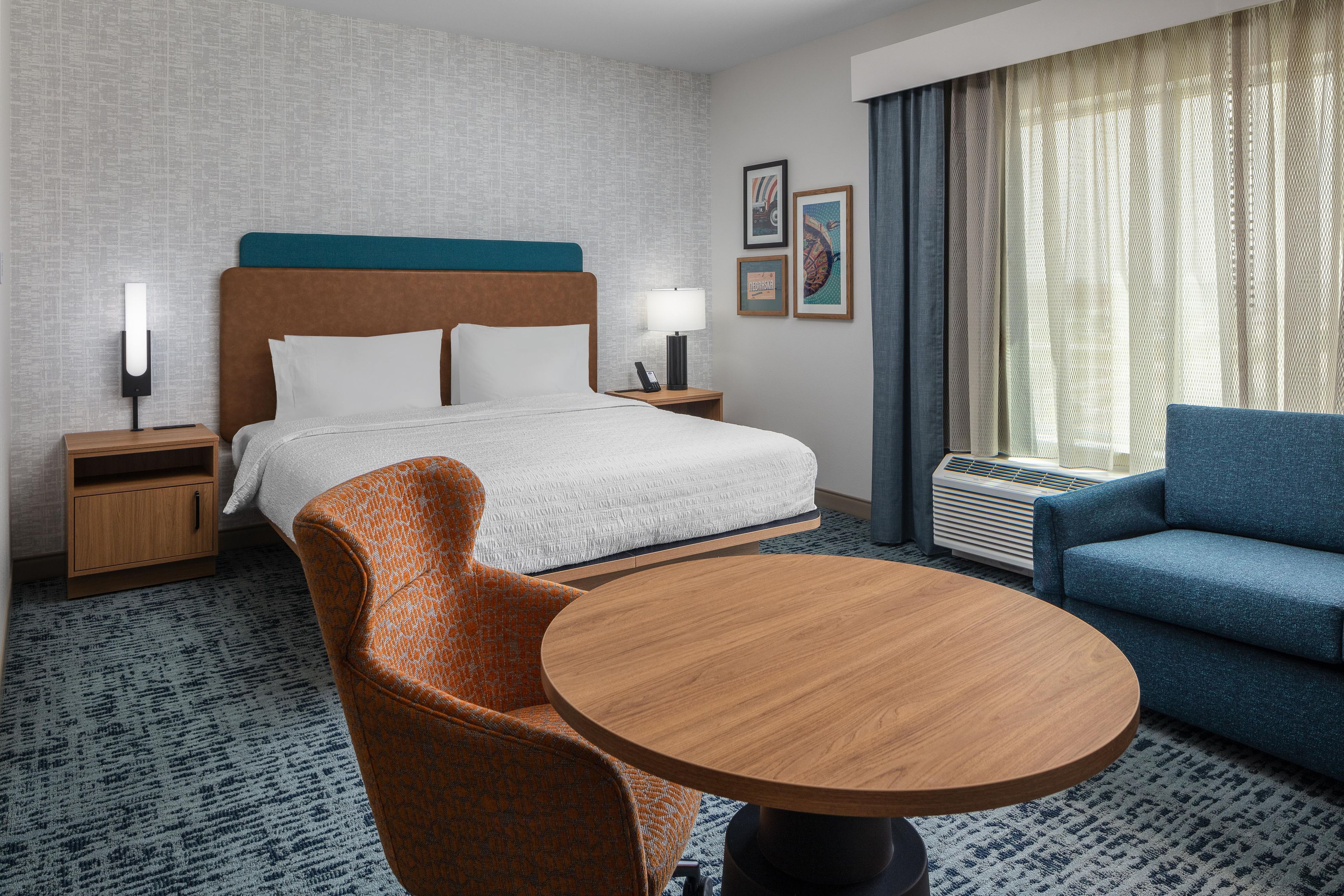 A hotel room with a bed, two bedside tables, a round wooden table, a blue sofa, and a patterned carpet.