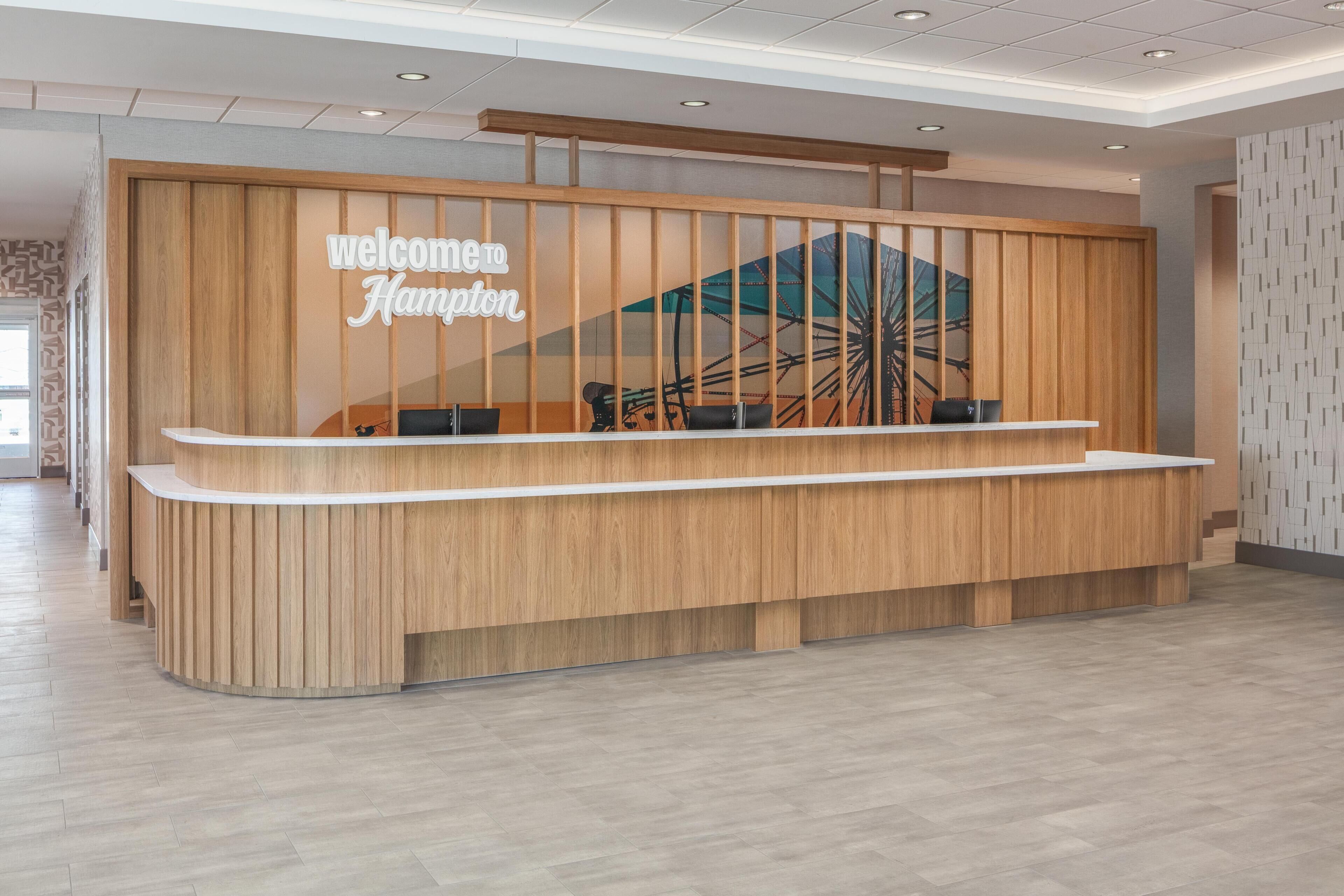 A reception desk with a 'Welcome Hampton' sign, a wooden panel design, and a view of a Ferris wheel through a window.
