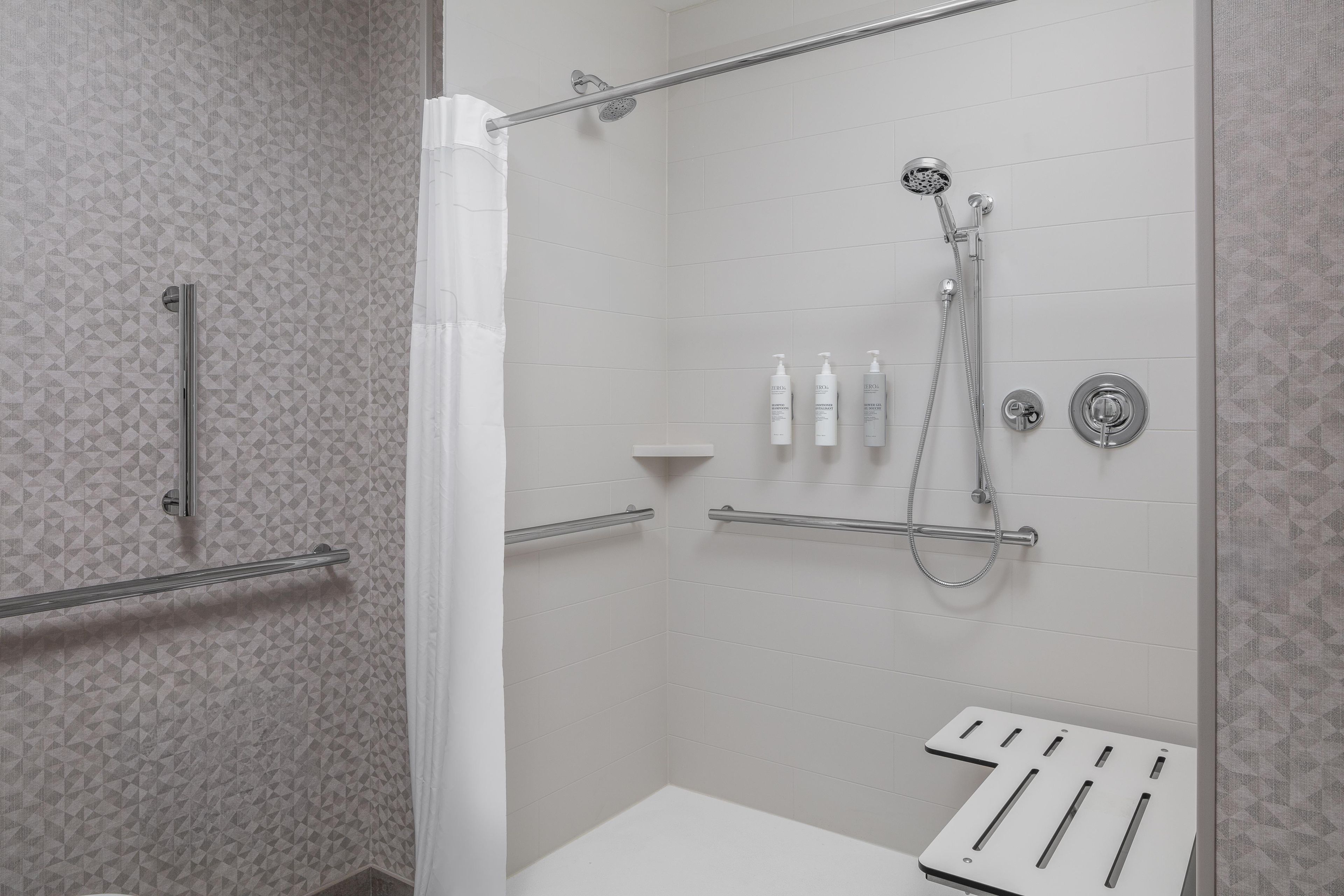 A modern shower area with a glass door, a handheld showerhead, a handheld showerhead, and a wall-mounted faucet.