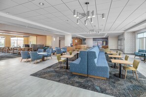 A modern hotel lobby with a long blue seating area, multiple tables, and a reception desk.