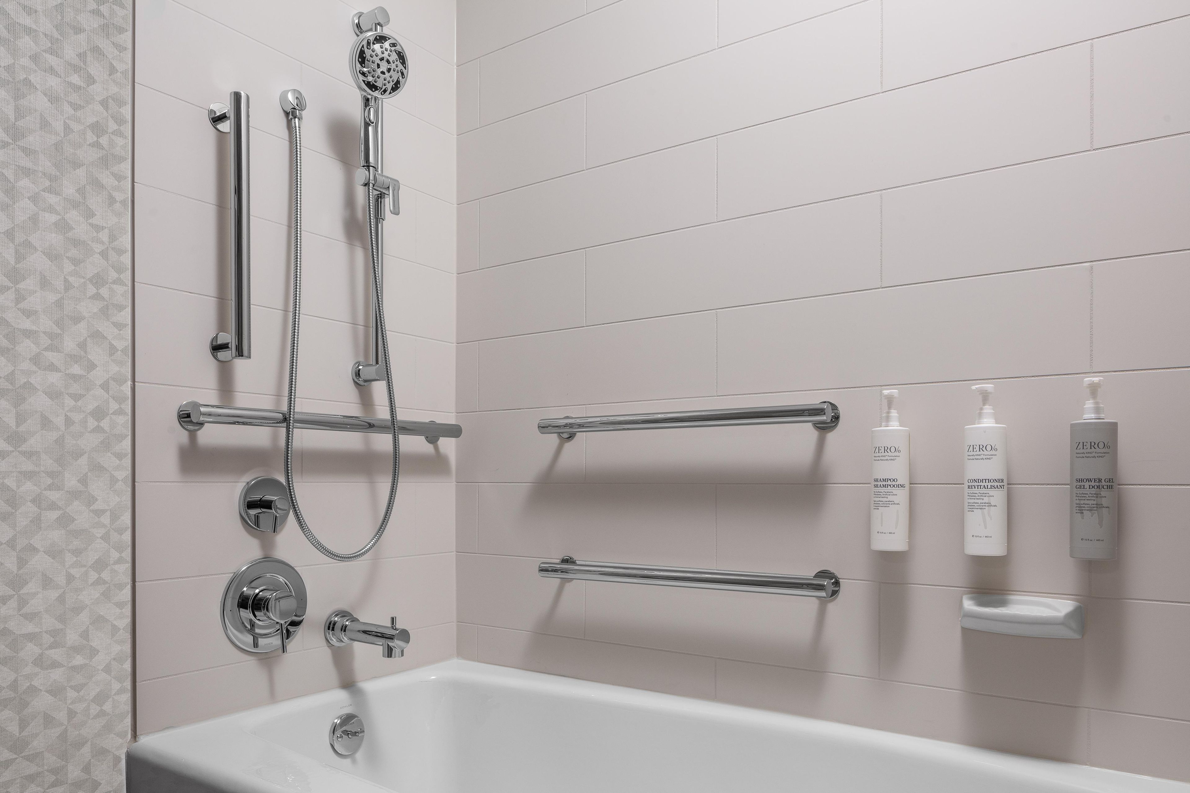 Une salle de bain moderne équipée d’une baignoire, d’une douche avec un pommeau de douche amovible et de toilettes fixées au mur.
