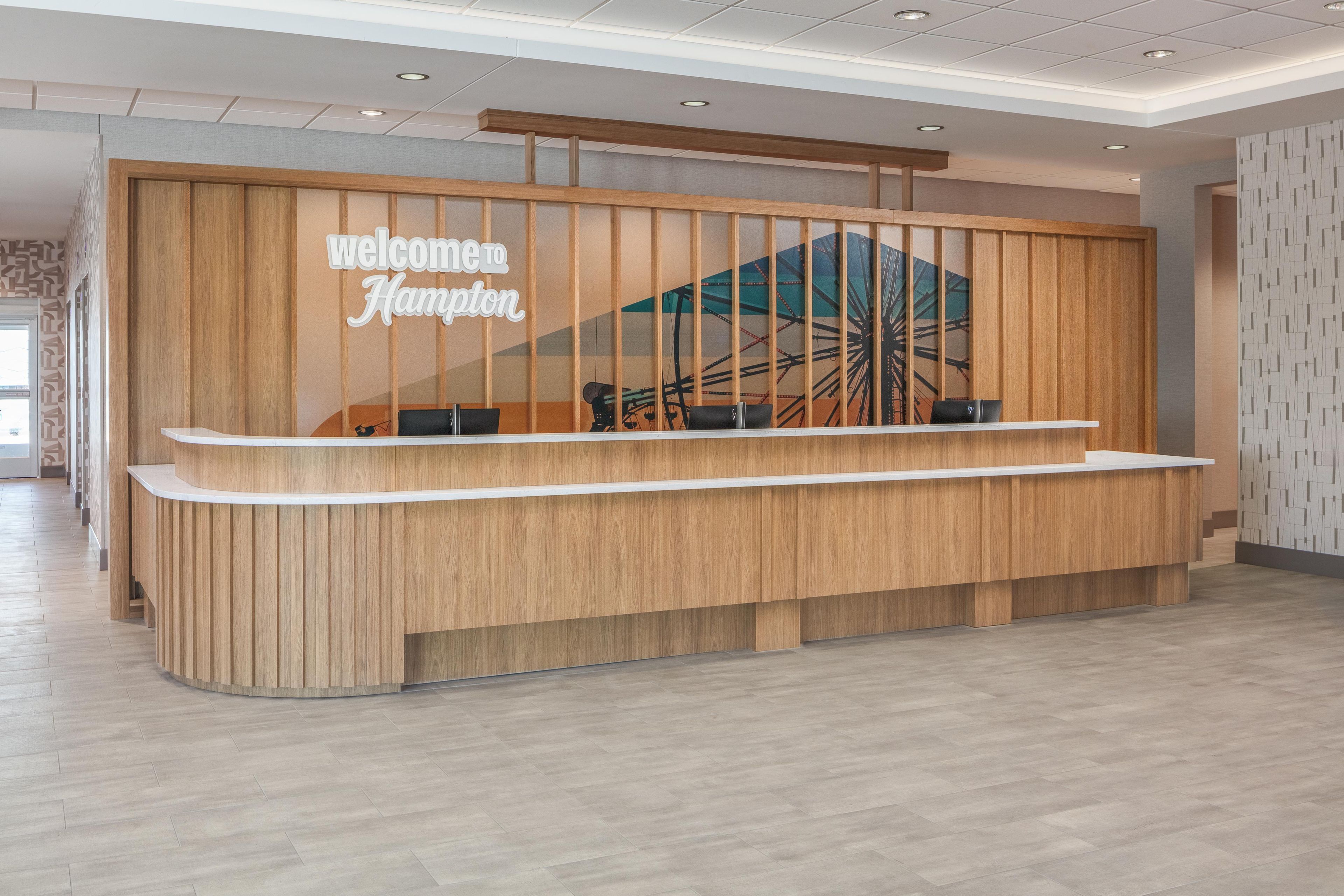 A reception desk with a 'Welcome Hampton' sign, a wooden panel design, and a view of a Ferris wheel through a window.