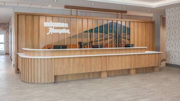 A reception desk with a 'Welcome Hampton' sign, a wooden panel design, and a view of a Ferris wheel through a window.