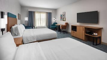 A hotel room with two beds, a desk, a chair, a TV, and a minibar.