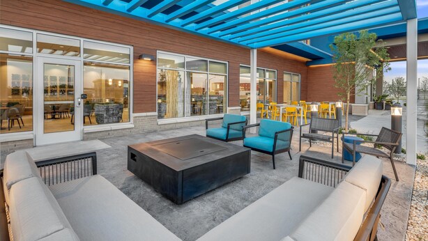 An outdoor patio with a fire pit, seating area, and large windows. - Hampton Inn by Hilton Grand Island Medical Center (Grand Island)