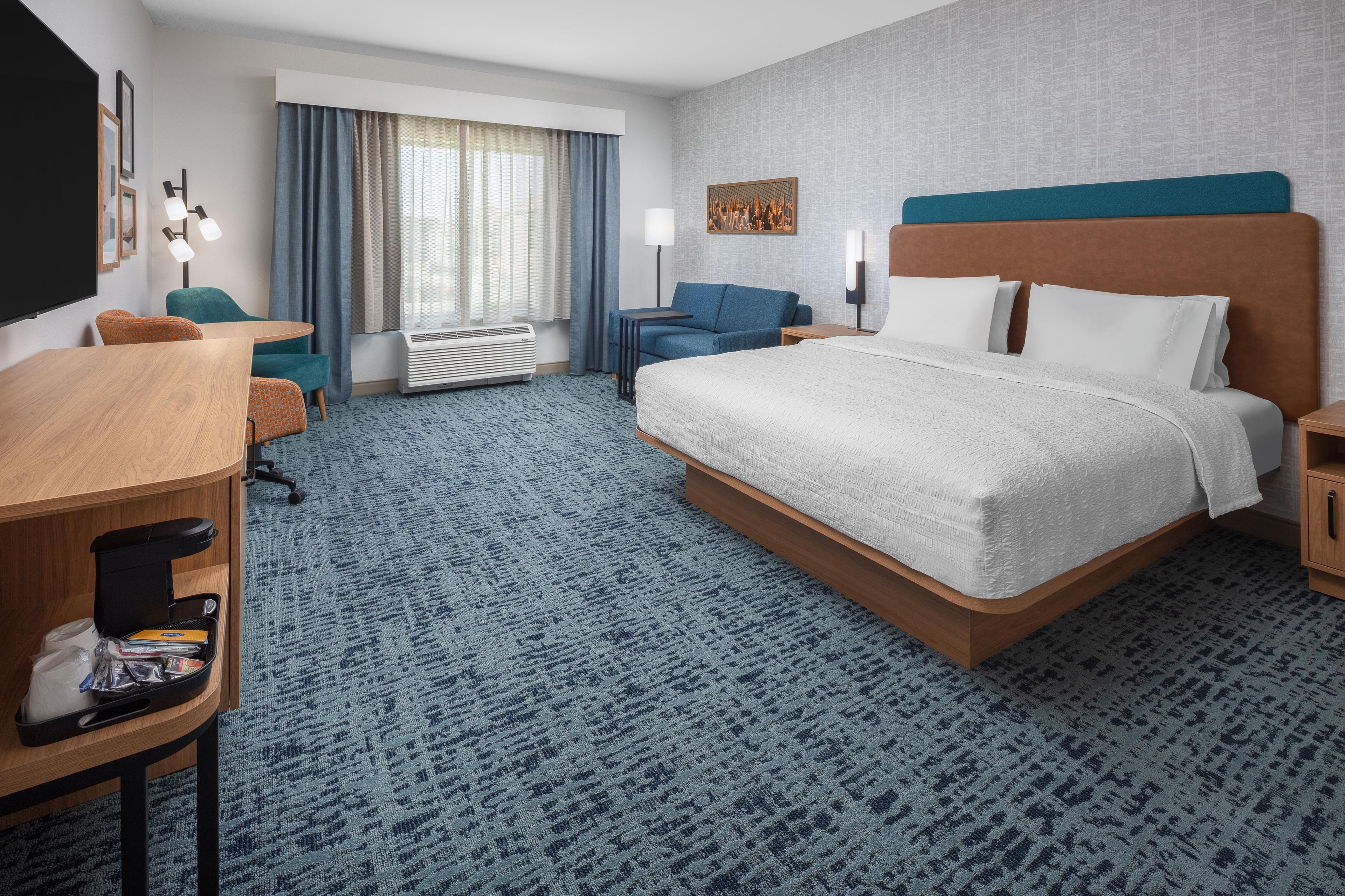 Een hotelkamer met een groot bed, een bureau, een stoel, een bank en een raam met gordijnen.