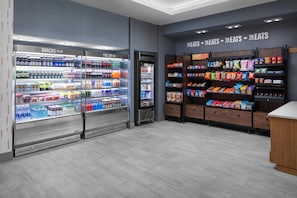 Interior de una tienda de comestibles con secciones refrigeradas de snacks y combustibles, y estantes llenos de diversas opciones de bocadillos y dulces.