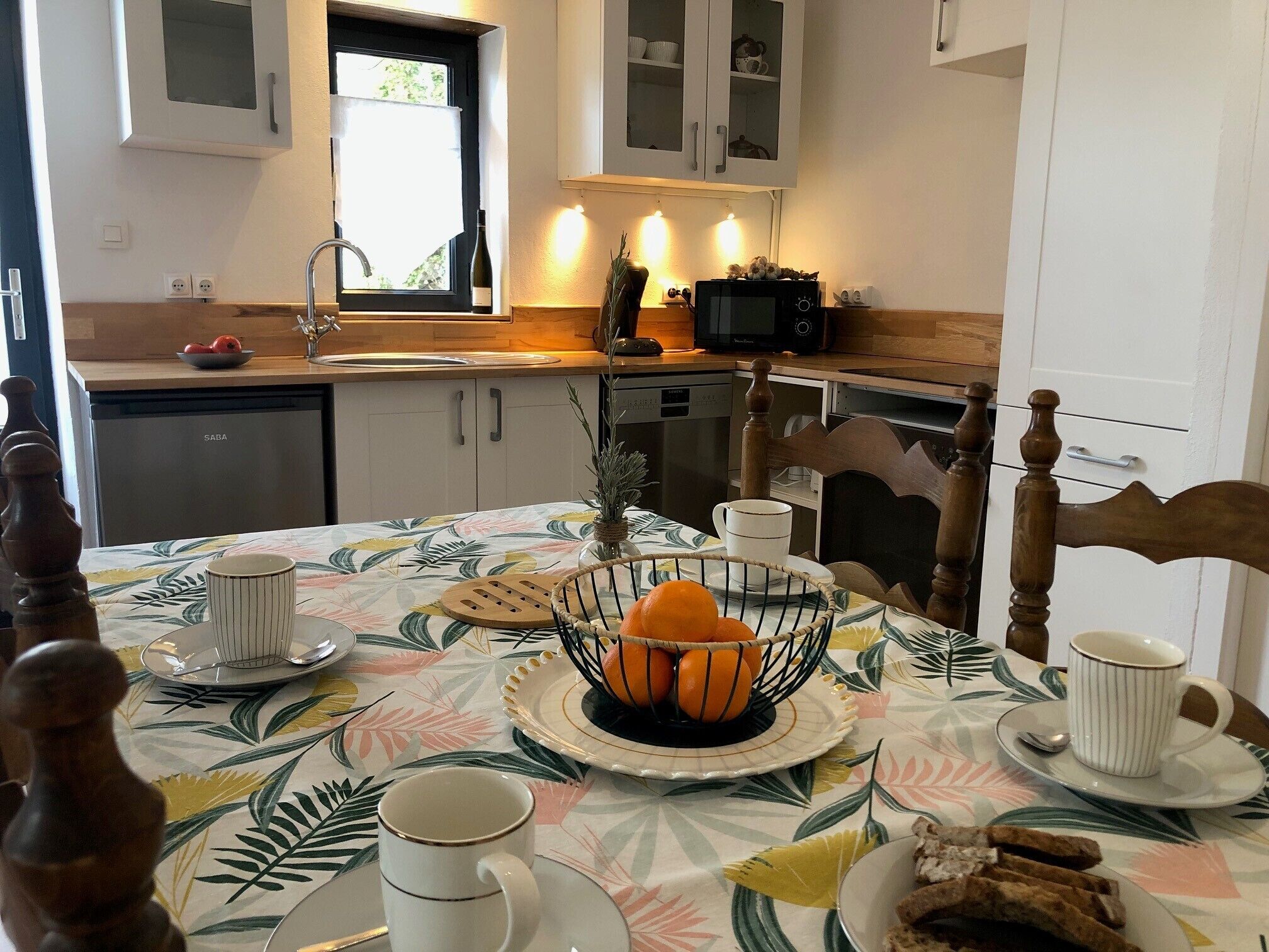 Ein Essbereich mit Tisch für zwei Personen, ausgestattet mit Obstschale, Tellern, Tassen und einer Kaffeekanne.