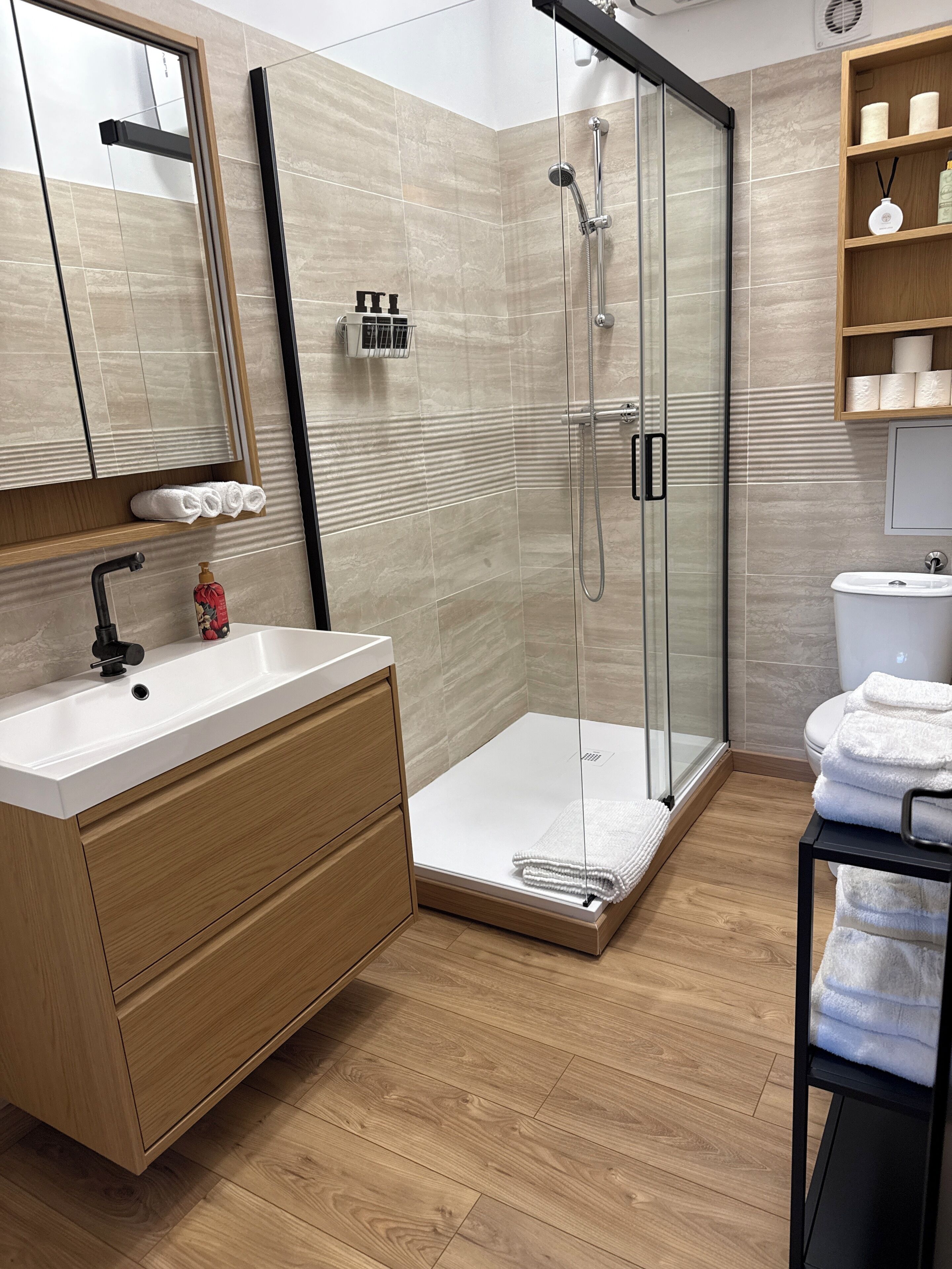 A modern bathroom with a glass shower enclosure, a wooden vanity with a sink, and a toilet.