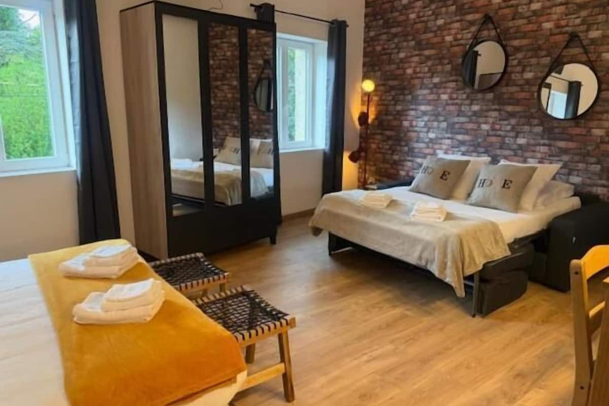 Ein Zimmer mit einem Bett, einem Tisch mit Handtüchern, einem Stuhl, einem Schrank und einer Backsteinwand.