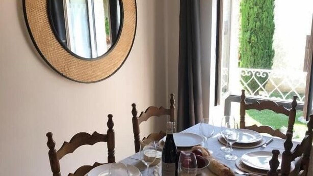 Une table à manger dressée avec des assiettes, des verres et une bouteille, entourée de chaises en bois.