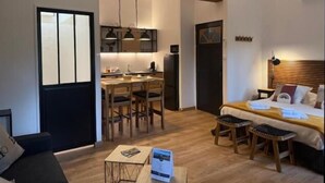 Un espace de vie compact comprenant un coin cuisine, un coin repas, un lit avec une tête de lit et un coin salon.
