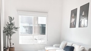 Ein modernes Wohnzimmer mit großem Fenster, einem grauen Teppich mit Muster, einem weißen Sofa und einem kleinen Couchtisch.