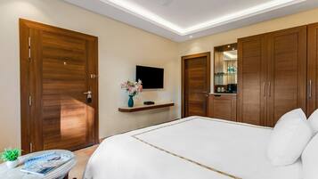 Habitación de hotel con una cama grande, armarios de madera, televisor montado y una mesita con planta y revista.