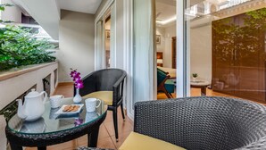 A balcony with a glass table, wicker chairs, a white teapot, and a vase with a purple flower. - Masaka Suites A Unit Of Arbat Hospitality LLP (Betalbatim)