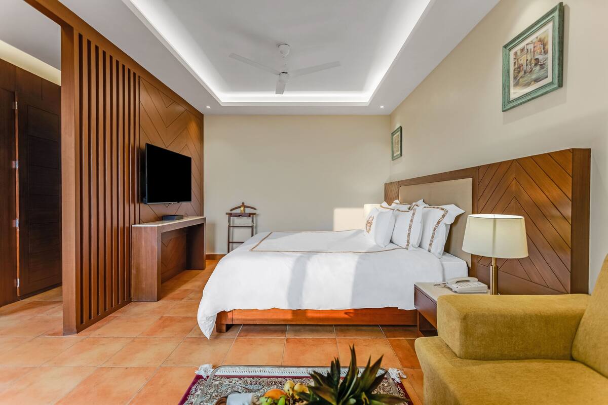 A hotel room with a bed, a desk, a TV, a lamp, and a chair.