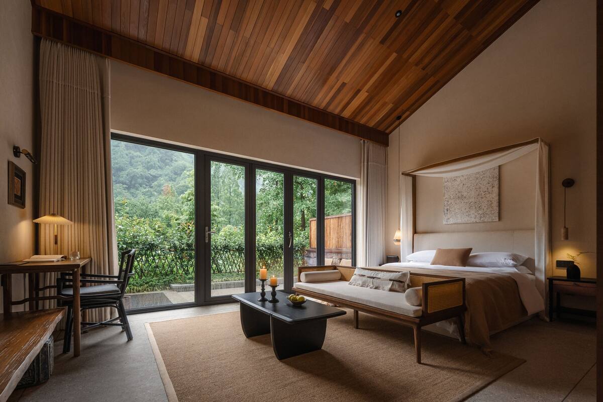 A modern bedroom with a large window, a bed, a sofa, a table, and a chair.