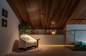 Una camera accogliente con soffitto in legno, una poltrona comoda, un tavolino, una pianta e un vano vetrato con vista.
