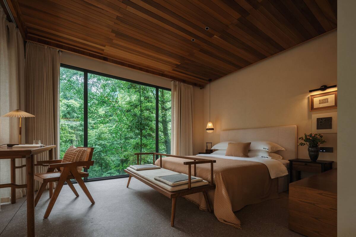 A modern bedroom with a large window, a bed, a bedside table, a chair, and a desk.