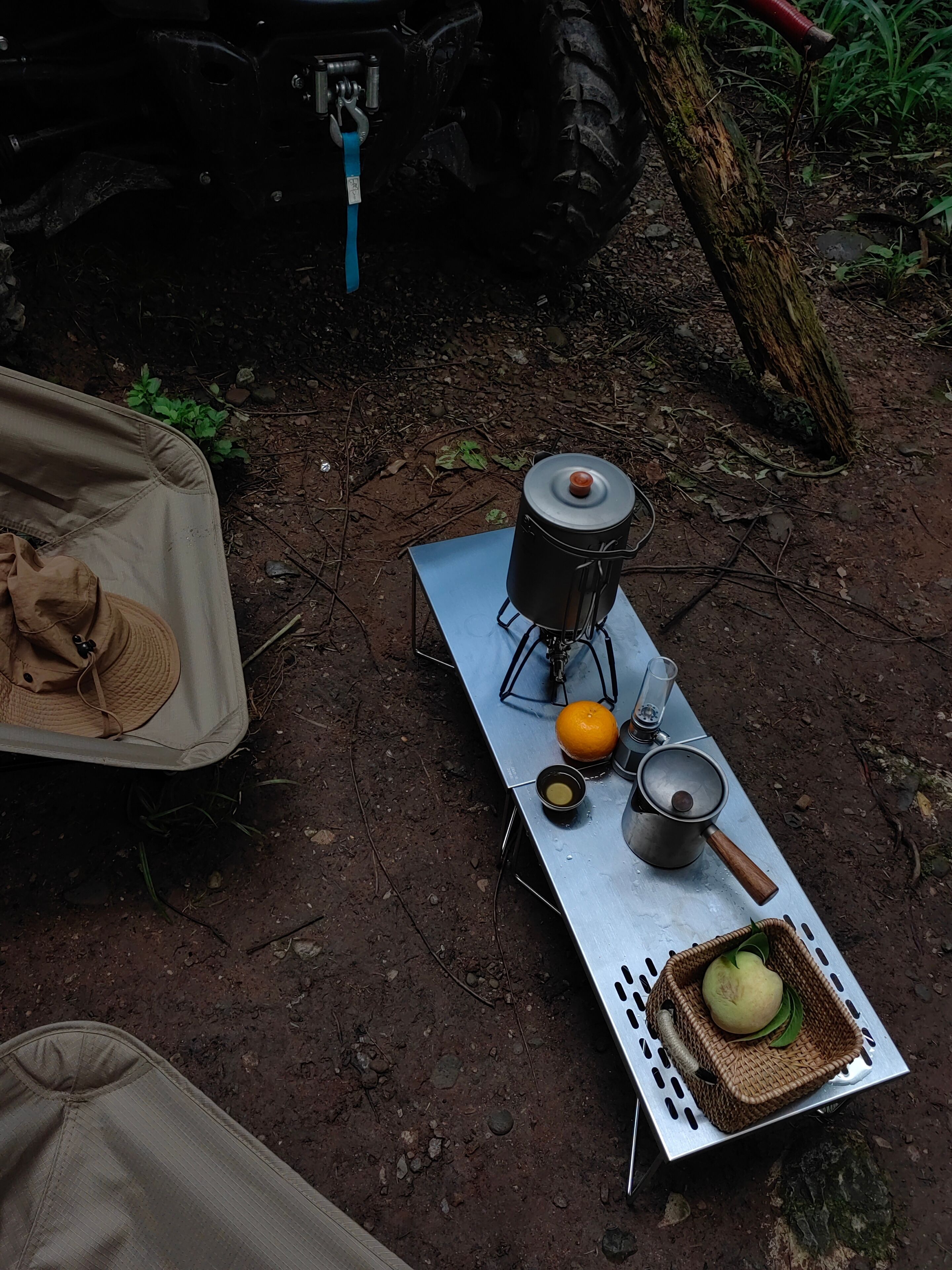 A camping setup with a portable stove, cooking pot, and a basket with a fruit.