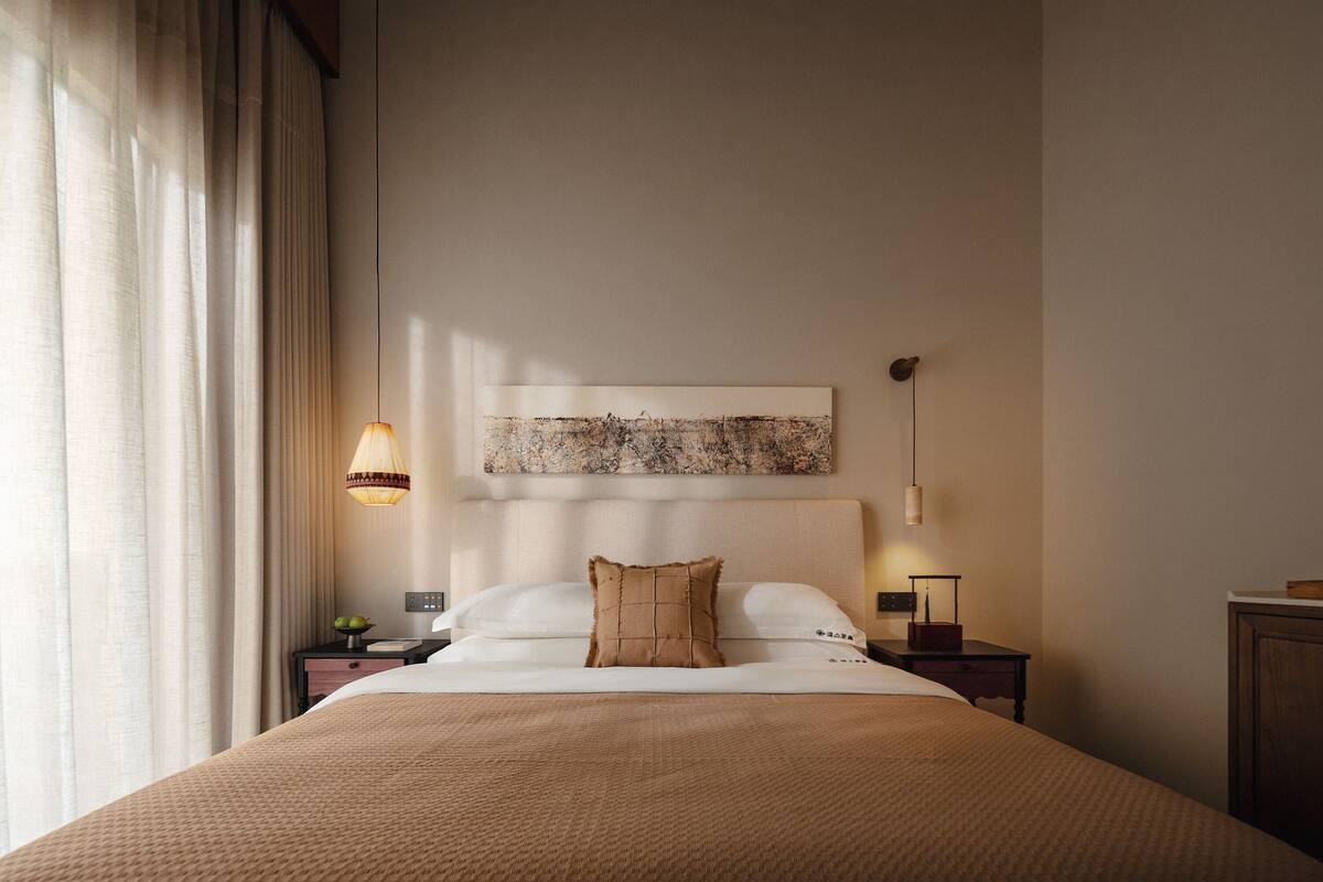 A hotel room with a bed, a nightstand, a lamp, and a painting on the wall.