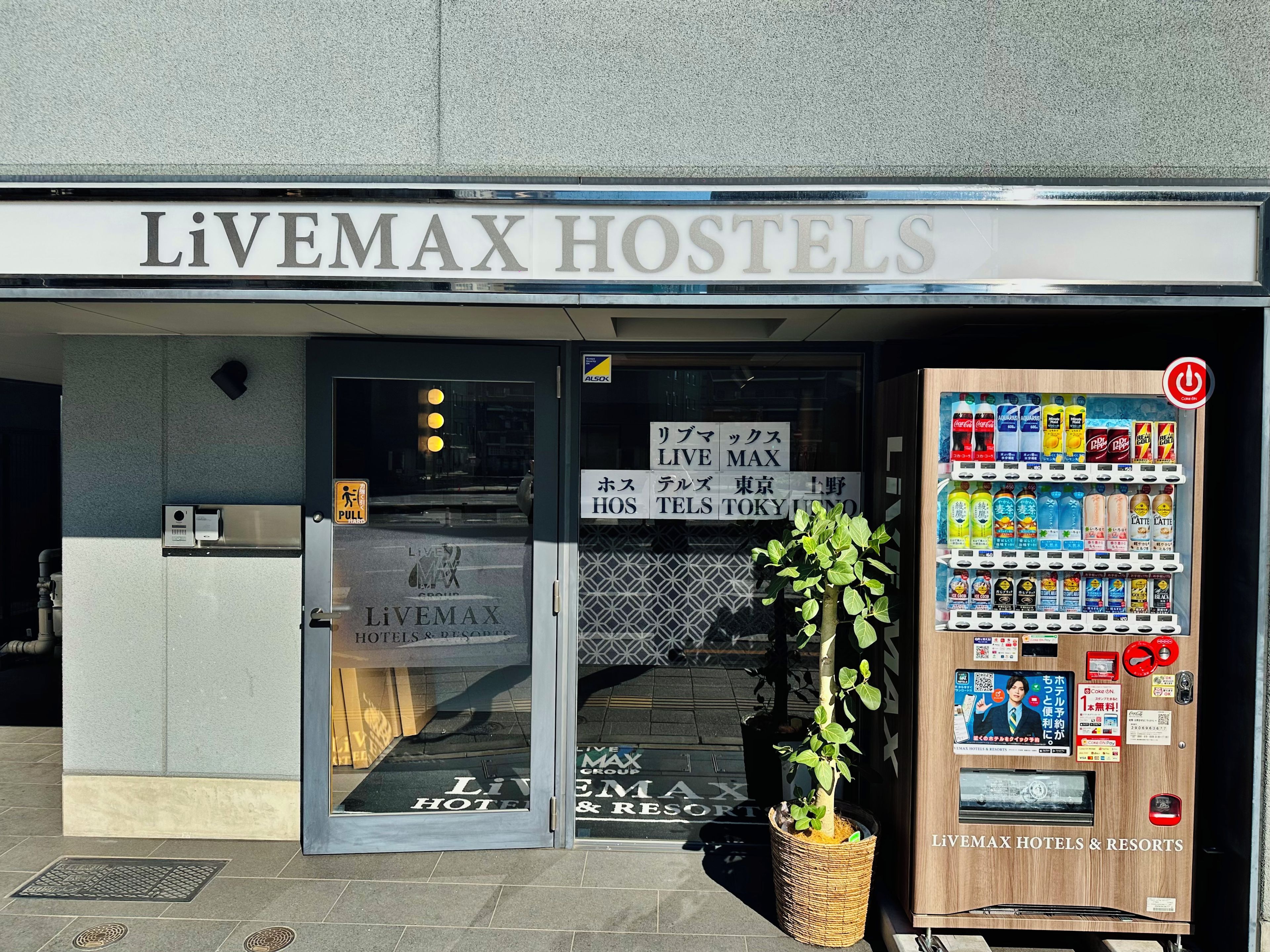 The entrance to Livemax Hostels with a vending machine and a sign indicating the hotel's name.