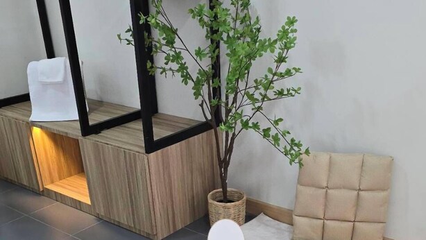 Un salon moderne avec une table basse en bois, deux fauteuils beiges à coussins, une table d’appoint blanche et une plante en pot.