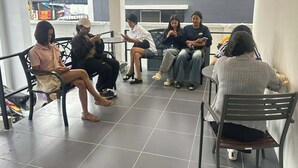 Un groupe de personnes est assis à des tables dans un espace extérieur d’un café, avec un sol carrelé et des chaises en métal.