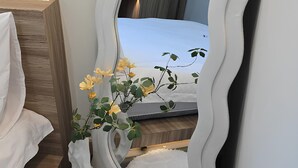 Une chambre avec un grand miroir, un lit, une table de chevet avec une lampe, un tapis blanc et moelleux, et un panier de pommes.