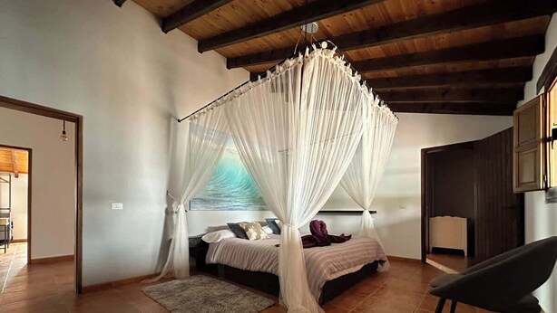 Un dormitorio con cama con dosel, una silla y vista al mar a través de la ventana.