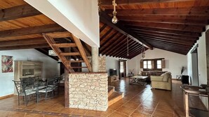 Un salón amplio con un pilar de piedra, vigas de madera, una mesa de comedor con sillas, un sofá y una televisión.