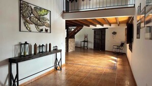 Un interior espacioso con techo alto, una escalera que conduce a un nivel superior y una larga consola decorada con objetos ornamentales.