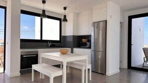 Una cuina moderna amb armaris blancs, electrodomèstics d'acer inoxidable i una zona de menjador amb taula i banc de color blanc.