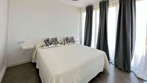Un dormitori amb un llit, una taula de nit, una làmpada i una finestra amb cortines.