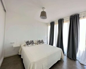 Ein Schlafzimmer mit einem Bett, einem Nachttisch, einer Lampe und einem Fenster mit Vorhängen.