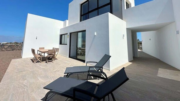 Una casa moderna de dos pisos amb un pati que disposa d'una taula, cadires i una cadira relaxant.