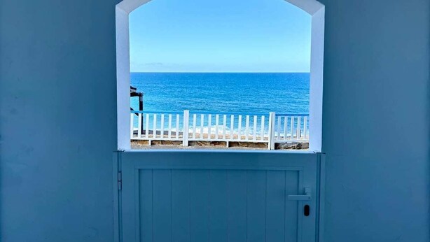 A view through a window with a white frame, overlooking a beach with a white fence and the sea. - House on the beach  WIFI Ajuy Fuerteventura (Ajuy)