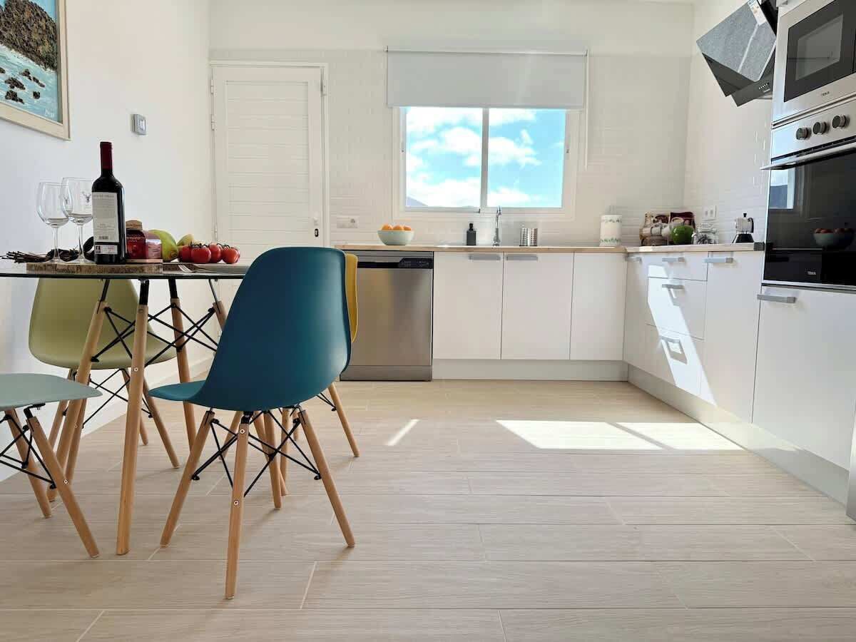 A modern kitchen with white cabinets, a dishwasher, and a window with a view of the sky.