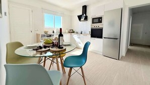 A modern kitchen with white cabinets, a stainless steel refrigerator, and a built-in oven. There is a dining area with a glass table and two chairs. - House on the beach  WIFI Ajuy Fuerteventura (Ajuy)