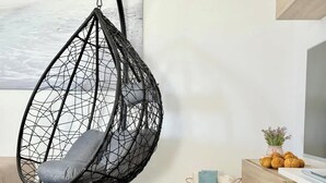 A black wire egg chair with a grey cushion in a modern living room with a wooden floor, a white sofa, and a wooden cabinet with a TV. - House on the beach  WIFI Ajuy Fuerteventura (Ajuy)