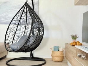Ein schwarzer Eiersessel mit grauem Kissen in einem modernen Wohnzimmer mit Holzboden, einem weißen Sofa und einer Holzkassette mit einem Fernseher.