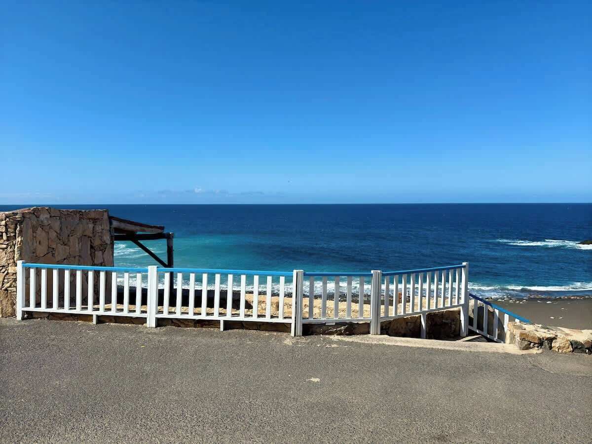 A coastal view with a white fence, a stone structure, and the ocean.