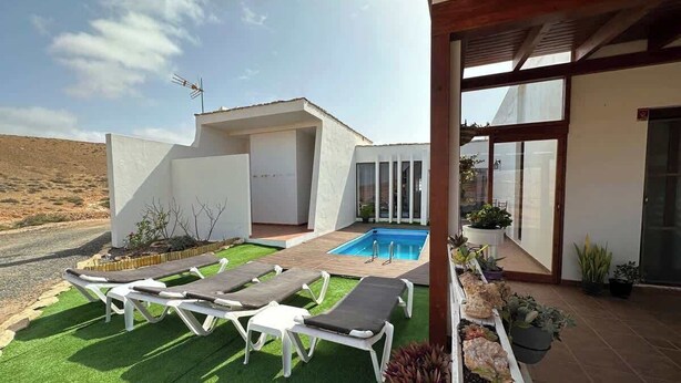 Una casa moderna con piscina, mobiliario exterior y un jardín bien cuidado.